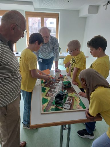 Kinder und Erwachsene spielen gemeinsam an einem Tisch mit einem Spielbrett.
