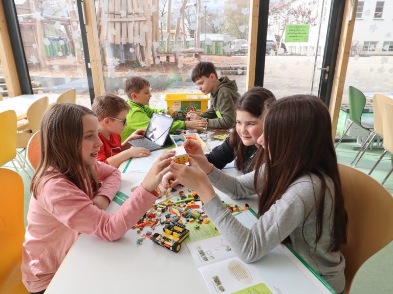 Kinder spielen gemeinsam mit LEGO und anderen Materialien in einem hellen Raum.