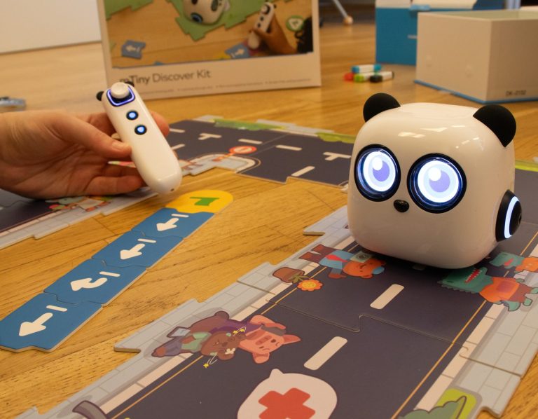 Ein kleiner, weißer Roboter mit großen leuchtenden Augen auf einem Spielteppich.