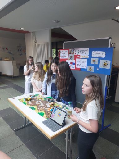 Schülerinnen präsentieren ein Projekt an einem Tisch in einem Foyer.